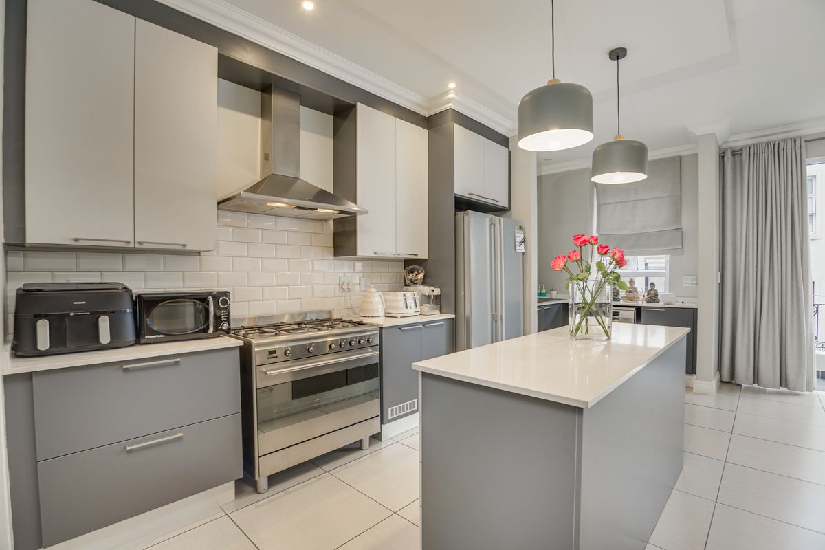 Modern kitchen featuring a central island, gas stove with extractor fan, subway tile backsplash, and sleek two-tone cabinetry with quartz countertops.