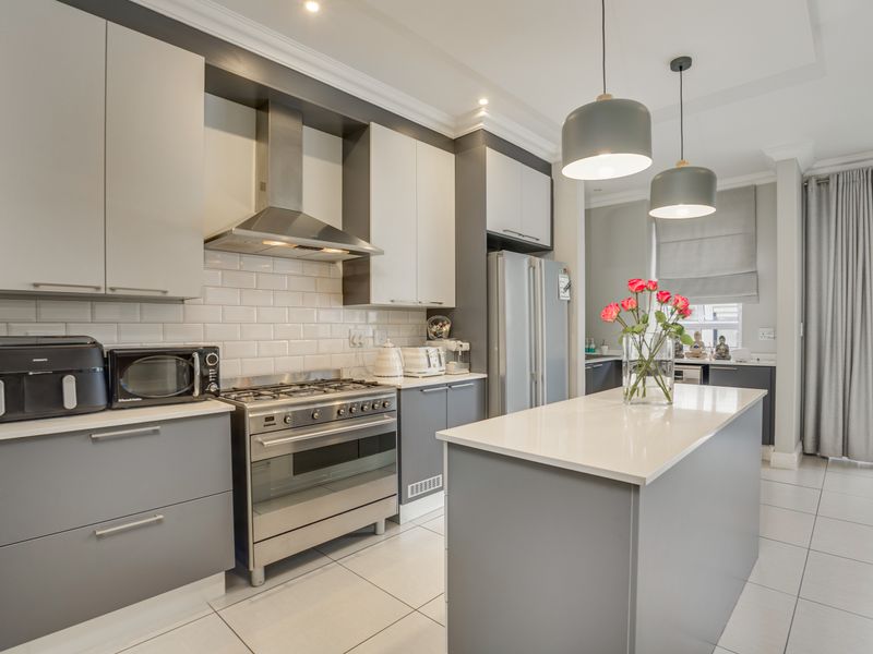 Modern kitchen featuring a central island, gas stove with extractor fan, subway tile backsplash, and sleek two-tone cabinetry with quartz countertops.