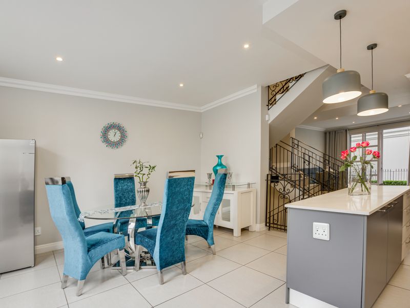 Modern open-plan dining and kitchen area featuring a central island, tiled flooring, recessed lighting, and an elegant wrought iron staircase.