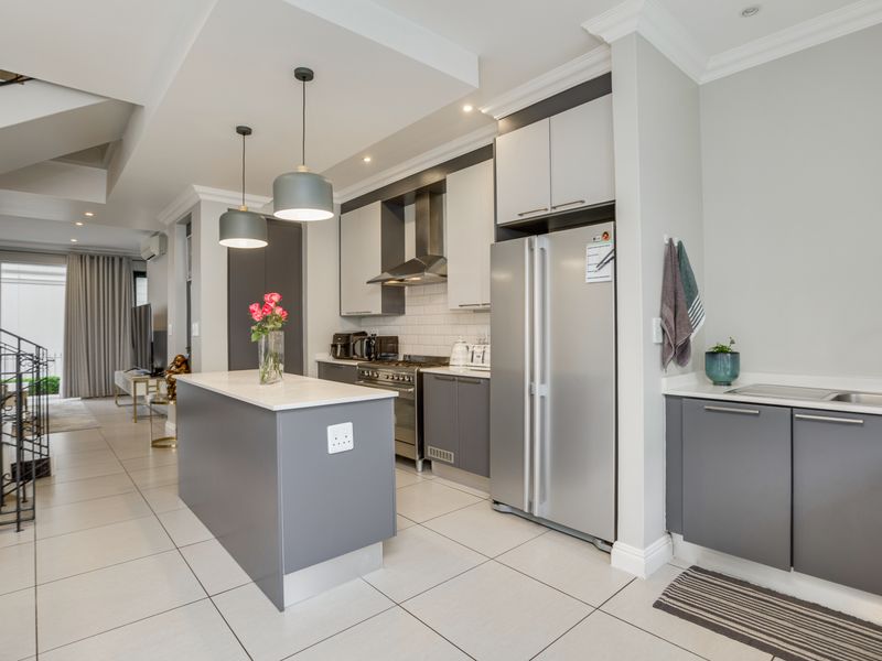 Modern open-plan kitchen featuring sleek grey cabinetry, a central island, stainless steel appliances, subway tile backsplash, and tiled flooring, seamlessly flowing into the living area.