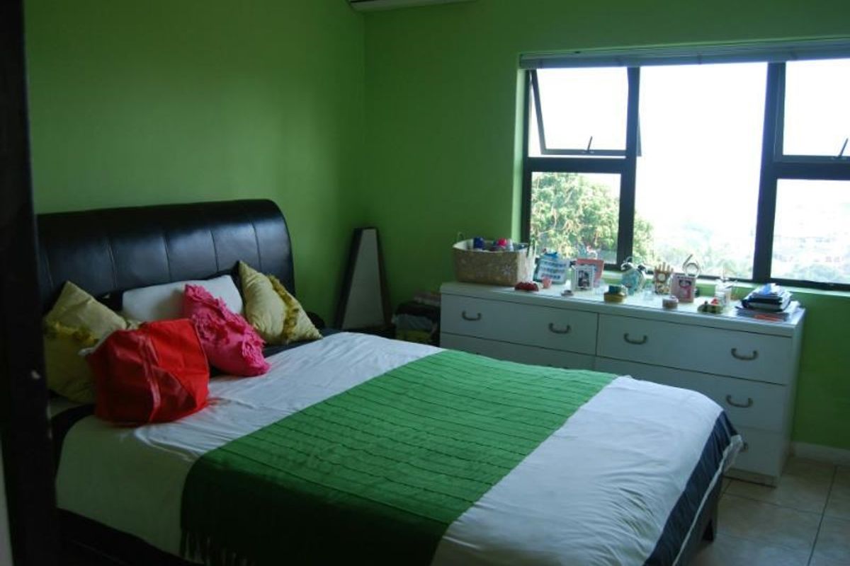 A bedroom featuring tiled flooring, aluminium window frames, and a wall-mounted air conditioning unit.