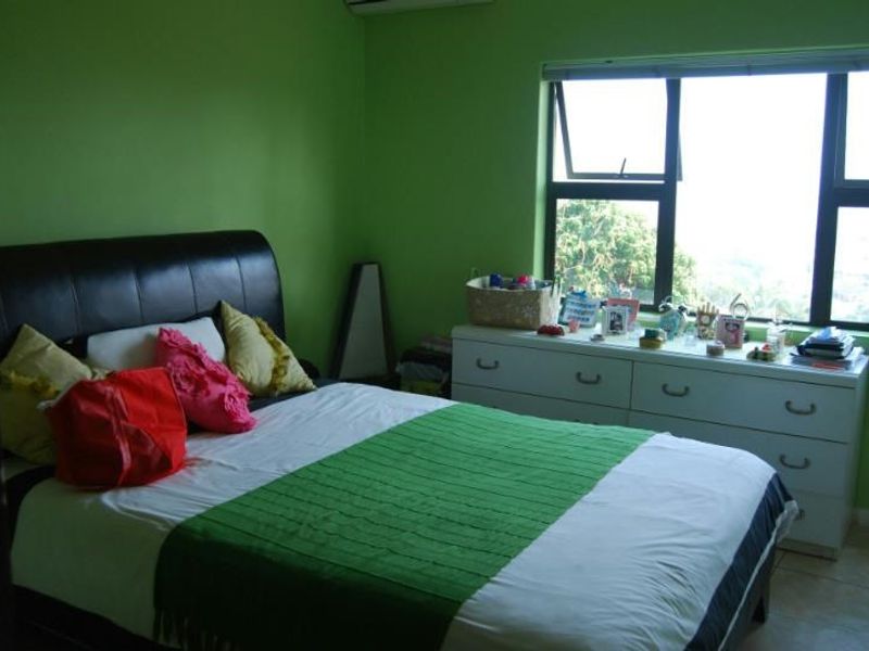 A bedroom featuring tiled flooring, aluminium window frames, and a wall-mounted air conditioning unit.