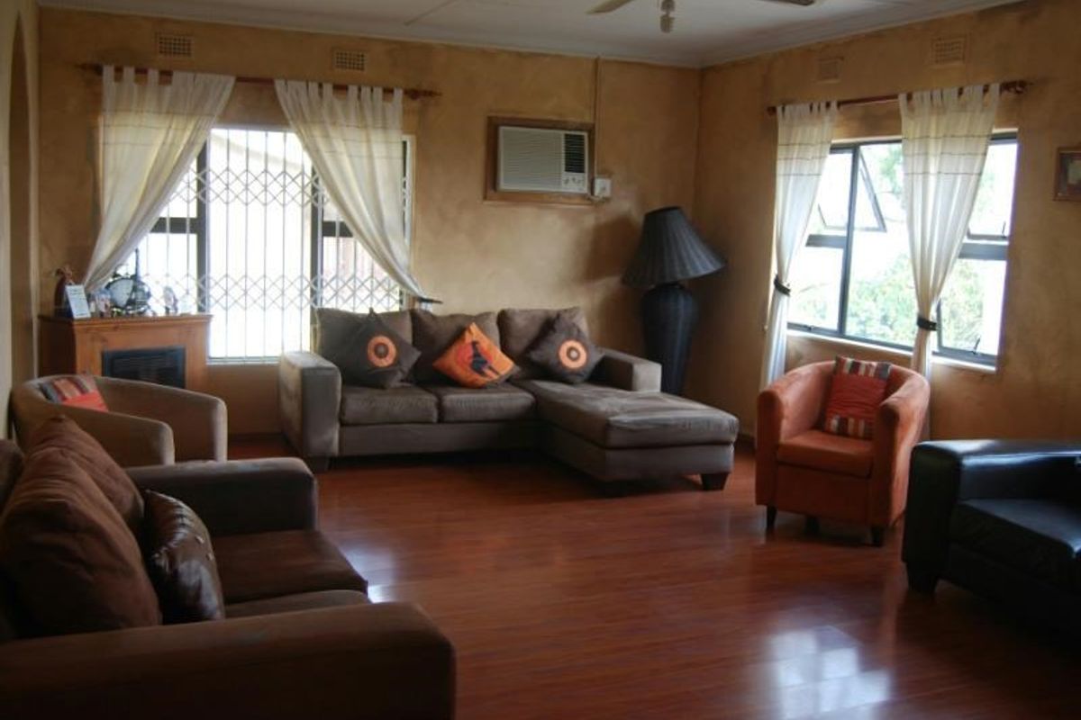 Spacious living room featuring laminate flooring, a built-in fireplace, and a wall-mounted air conditioning unit, with large windows fitted with security bars.