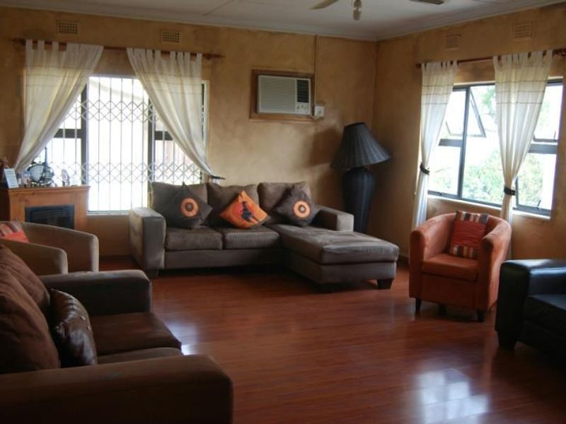 Spacious living room featuring laminate flooring, a built-in fireplace, and a wall-mounted air conditioning unit, with large windows fitted with security bars.