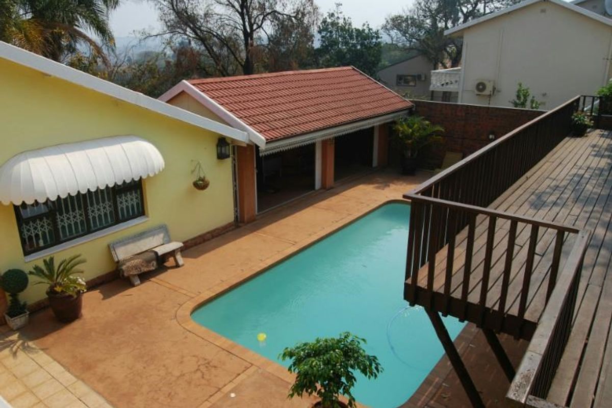 Outdoor pool area featuring a swimming pool, paved patio, and an elevated wooden deck with balustrades, providing a functional space for outdoor relaxation.