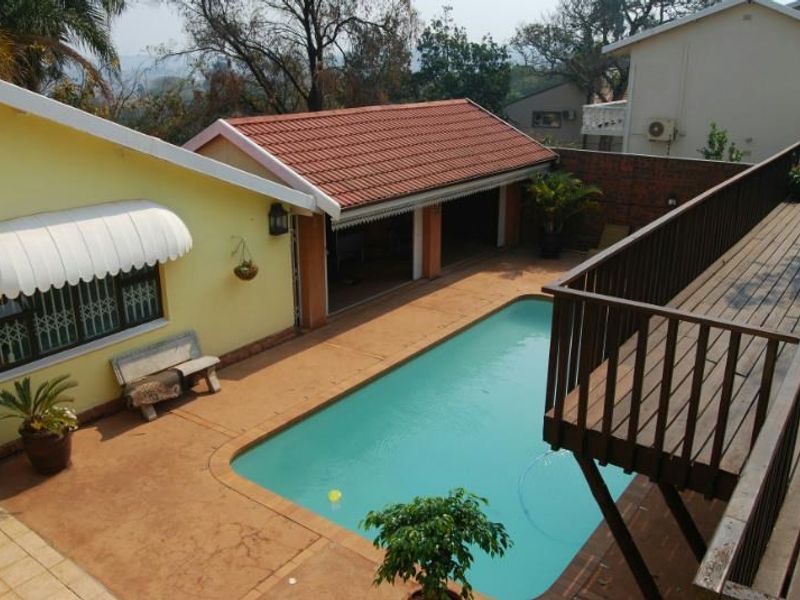 Outdoor pool area featuring a swimming pool, paved patio, and an elevated wooden deck with balustrades, providing a functional space for outdoor relaxation.