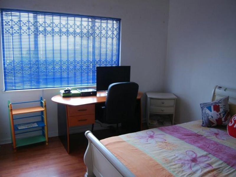 A functional bedroom featuring laminate flooring and blue security blinds on the window, providing a practical space for rest or study.