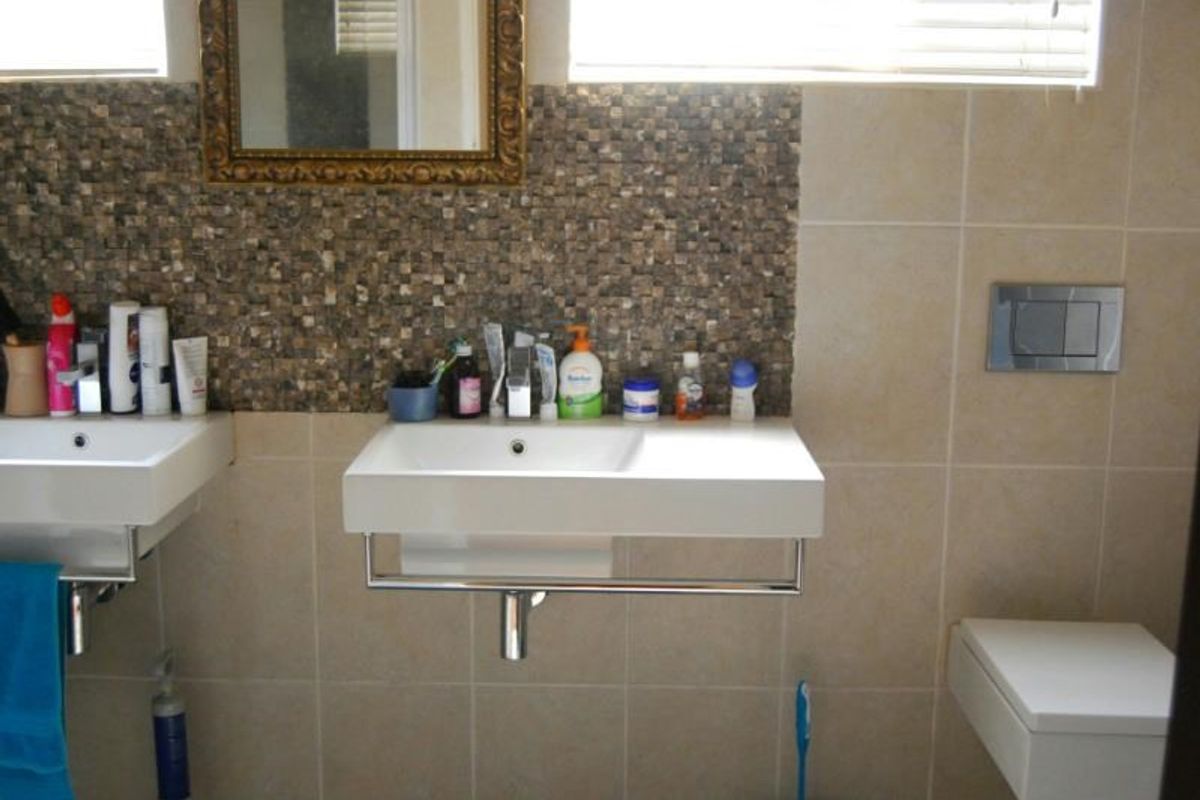A functional bathroom featuring dual wall-mounted basins, a mosaic tile feature wall, and a modern wall-mounted toilet with a chrome flush plate.