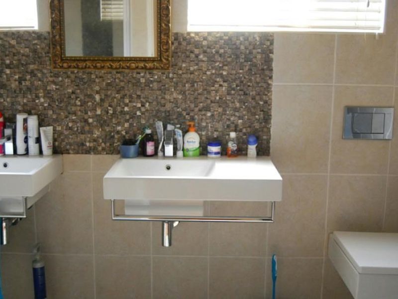 A functional bathroom featuring dual wall-mounted basins, a mosaic tile feature wall, and a modern wall-mounted toilet with a chrome flush plate.