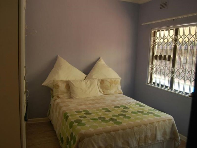 A standard bedroom featuring laminate flooring, a built-in wardrobe, and a window fitted with a security gate.