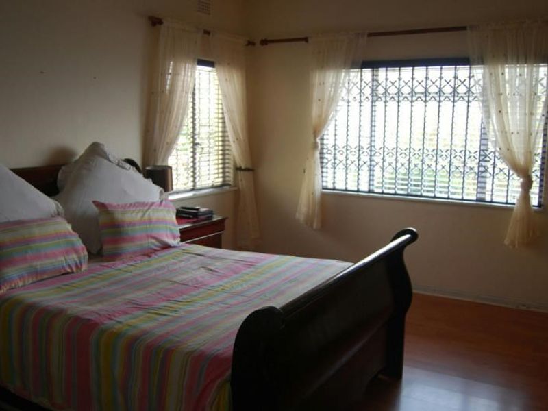 A standard bedroom featuring laminate flooring and windows fitted with security bars.