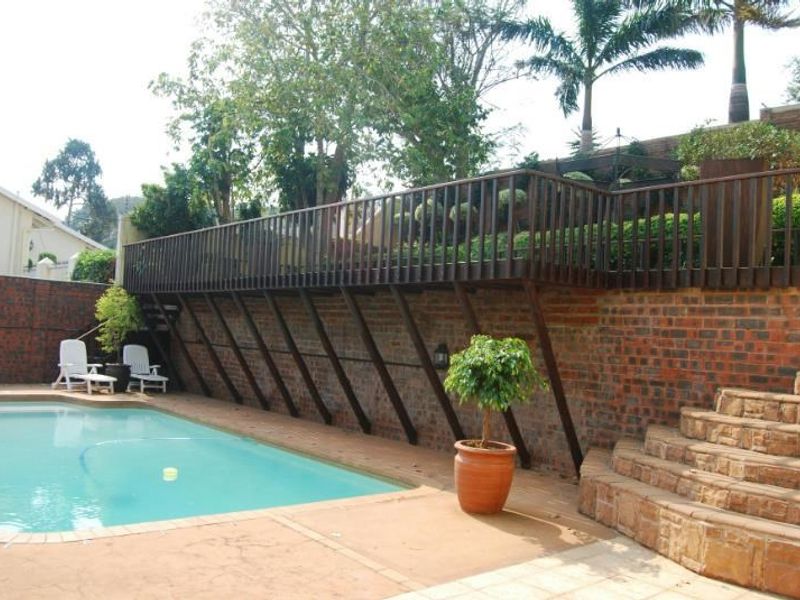 Outdoor pool area featuring a raised timber deck, brick retaining wall, and stone stairs leading to the upper garden level.