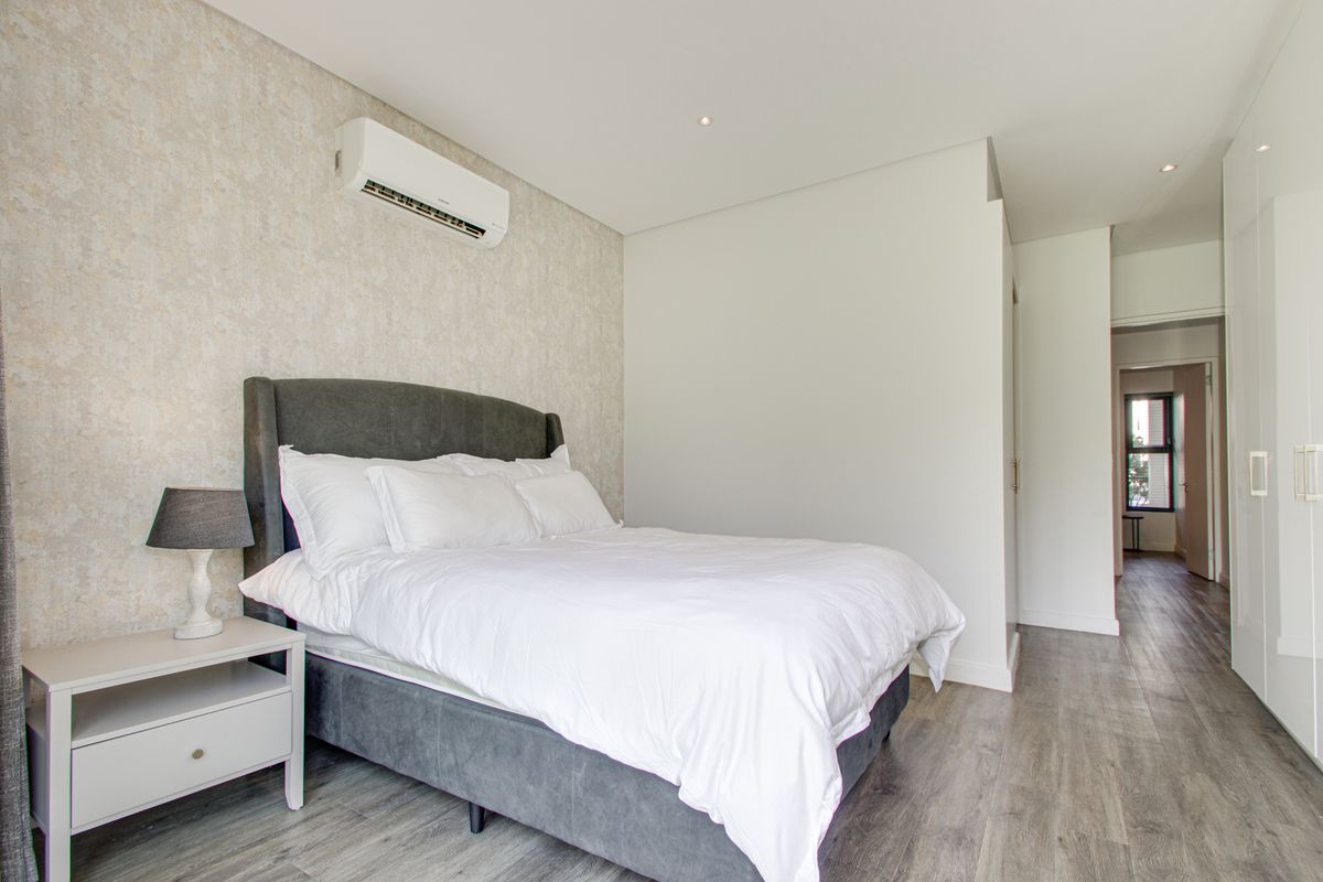 Modern bedroom featuring laminate flooring, built-in cupboards, textured feature wall, and a wall-mounted air conditioning unit.