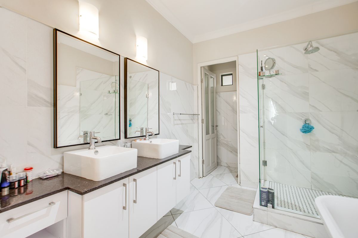 Modern bathroom featuring a double vanity with vessel sinks, marble-look wall tiles, and a glass-enclosed walk-in shower.