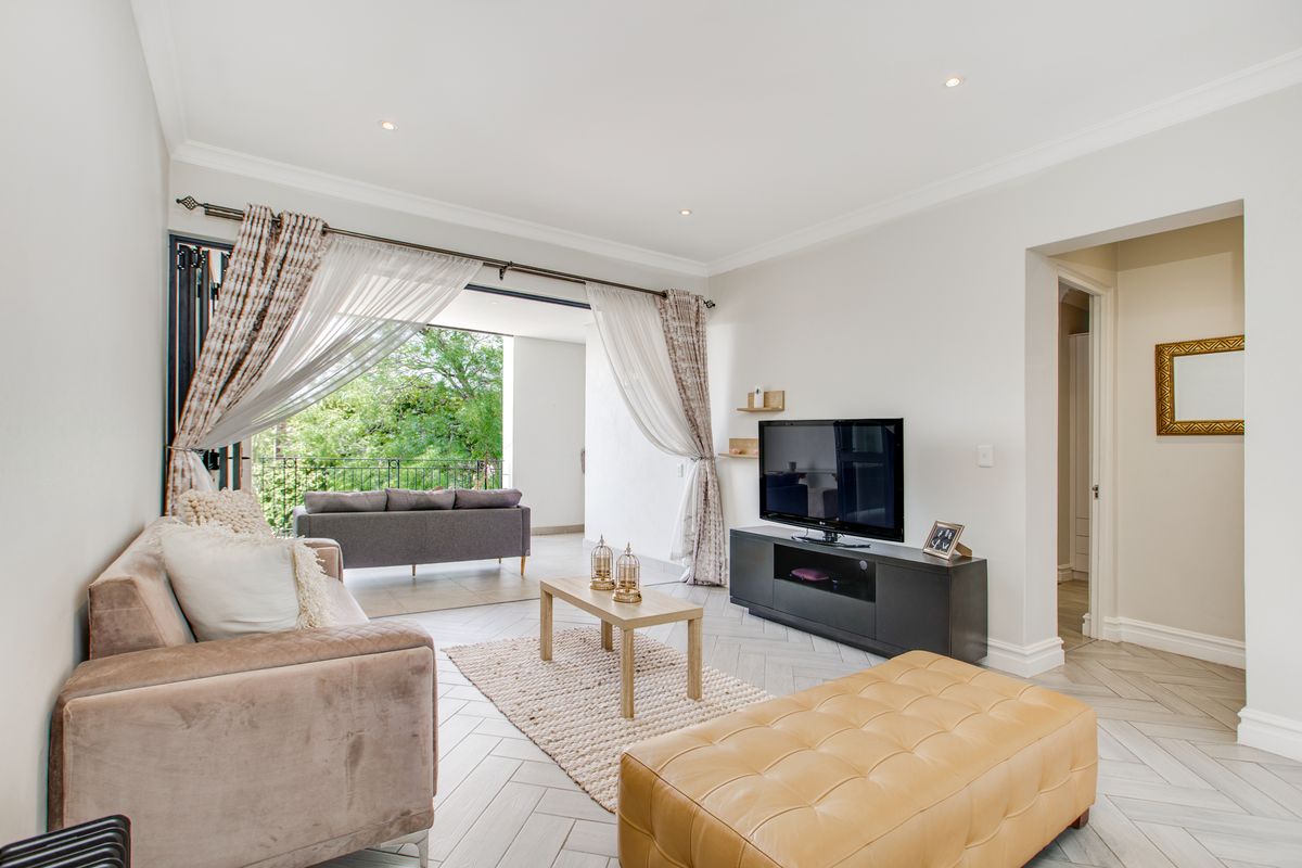 Bright living room featuring herringbone-patterned flooring, recessed ceiling lighting, and large sliding doors opening onto a private balcony with lush greenery views.