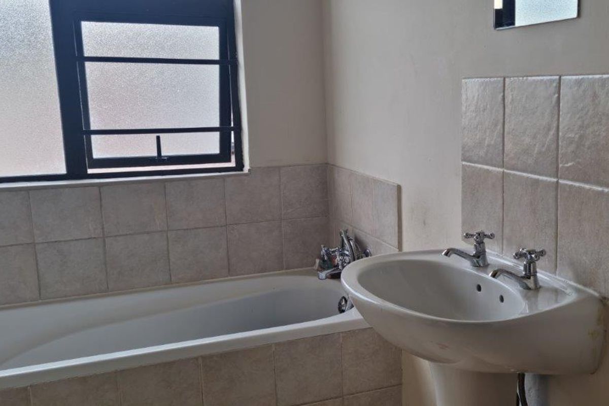 A functional bathroom featuring a standard bathtub with tiled surround and a pedestal washbasin with chrome taps.