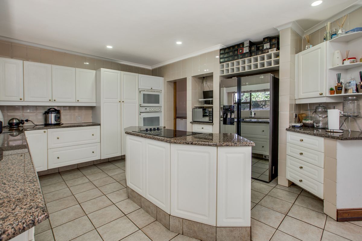 Spacious kitchen featuring white cabinetry, granite countertops, a central island with a built-in hob, and integrated wall ovens.