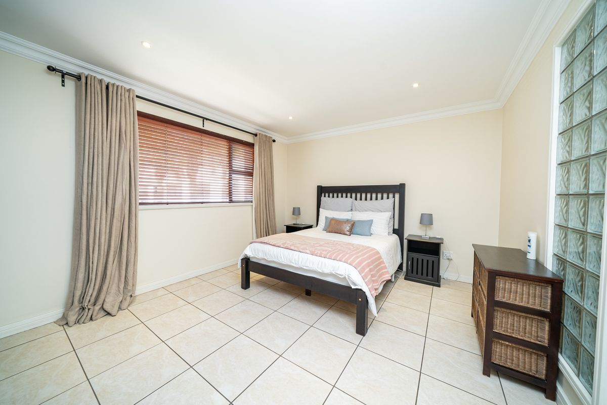 A well-maintained bedroom featuring neutral tiled flooring, recessed ceiling lighting, crown molding, and a distinctive glass block feature wall.