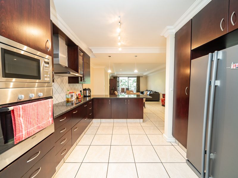 Modern open-plan kitchen featuring dark wood cabinetry, granite countertops, built-in oven, microwave, and tiled flooring, flowing seamlessly into the adjacent living and dining area.