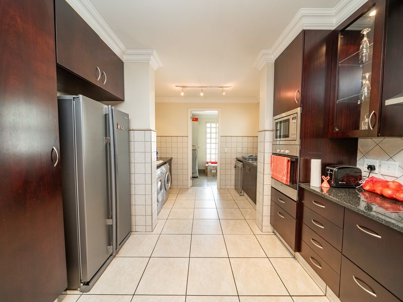 A functional kitchen featuring dark wood cabinetry, granite countertops, built-in oven, microwave, and a tiled floor, leading into a separate laundry area.