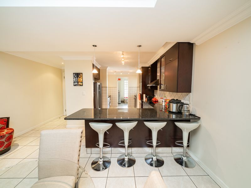 Open-plan kitchen featuring dark cabinetry, granite countertops, and a breakfast bar, seamlessly flowing into the living area with tiled flooring throughout.