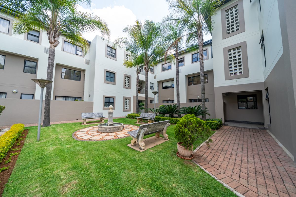 A well-maintained communal courtyard garden featuring a central fountain, paved walkways, and established palm trees within an apartment complex.