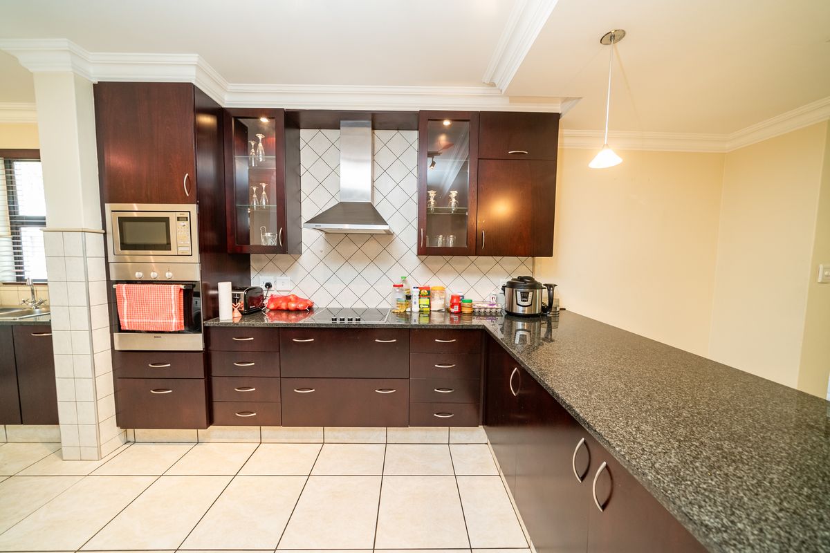 A well-maintained kitchen featuring dark wood cabinetry, granite countertops, a built-in oven, microwave, and a stainless steel extractor fan.
