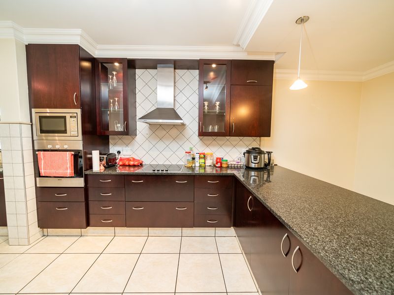 A well-maintained kitchen featuring dark wood cabinetry, granite countertops, a built-in oven, microwave, and a stainless steel extractor fan.