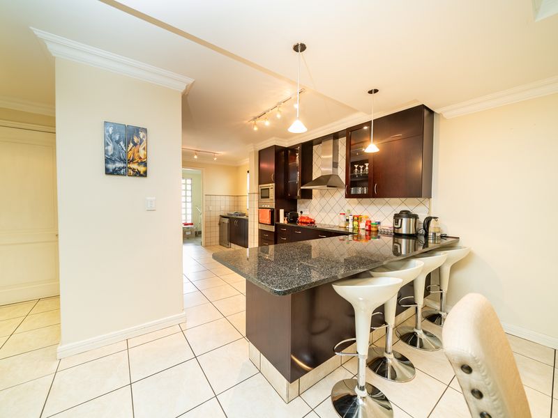 Modern open-plan kitchen featuring dark wood cabinetry, granite countertops, a breakfast bar, and integrated stainless steel appliances with tiled flooring throughout.