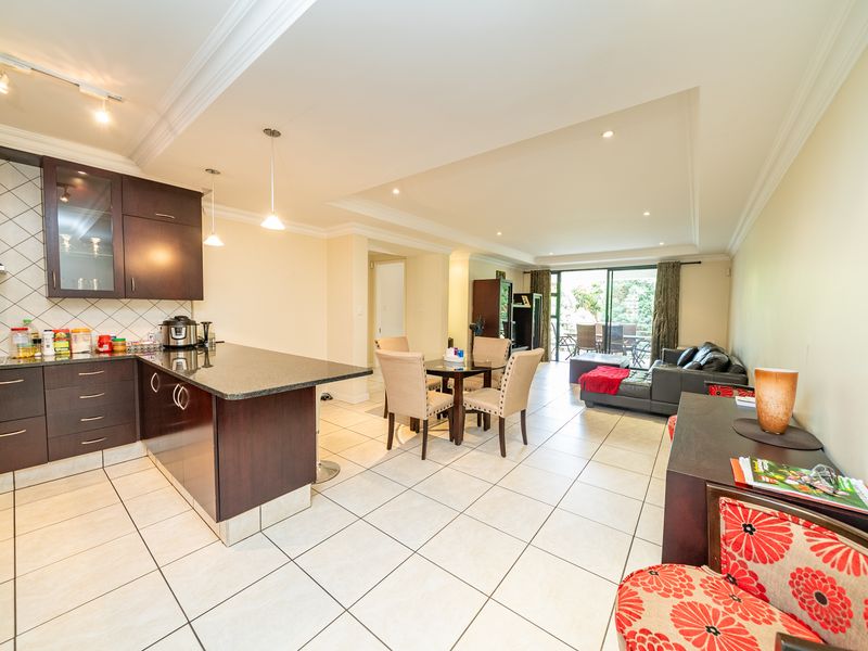 Open-plan living area featuring a modern kitchen with dark cabinetry, granite countertops, and tiled flooring, flowing into a dining space and lounge with balcony access.