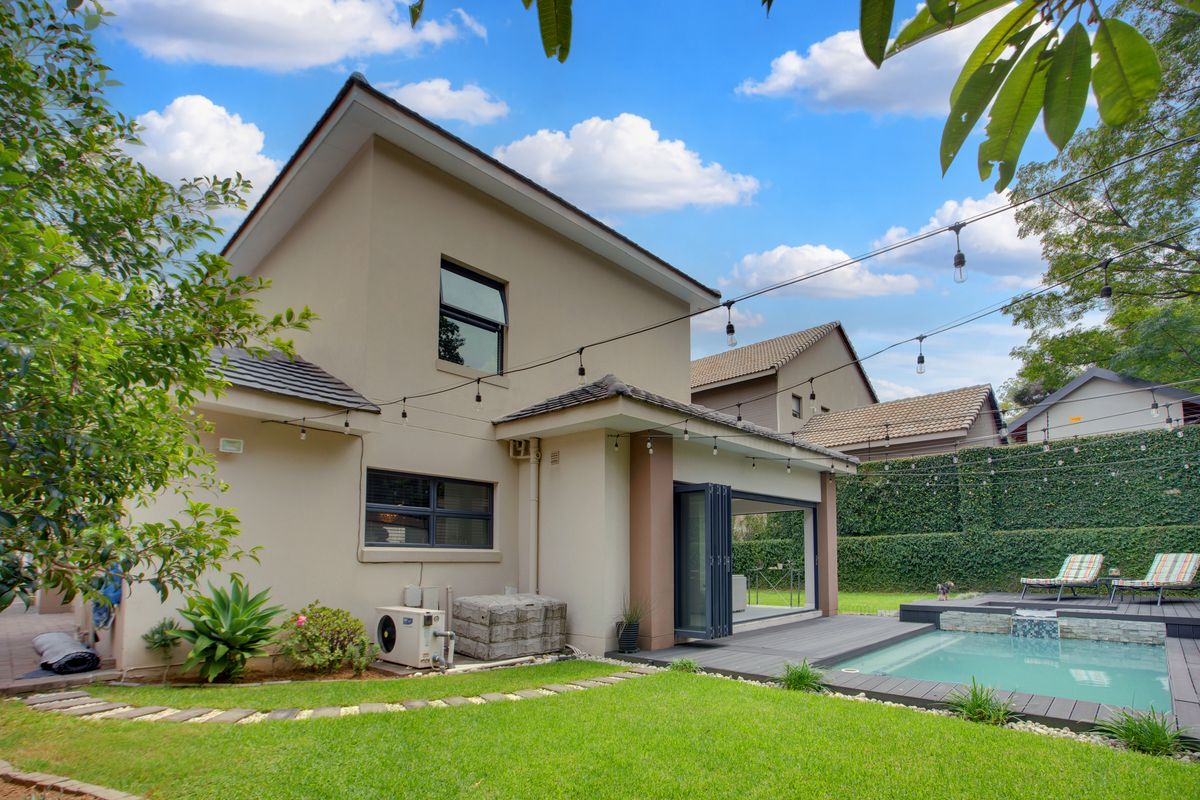 Rear view of the property featuring a swimming pool, timber decking, manicured lawn, and bi-fold doors leading into the living area.
