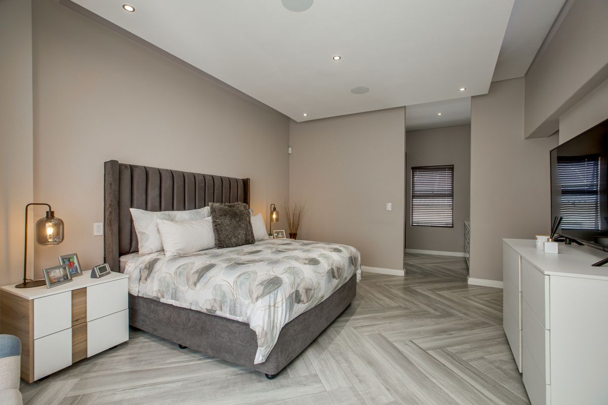 Spacious bedroom featuring modern herringbone-patterned flooring, recessed ceiling lighting, and a neutral color palette, creating a clean and contemporary living space.