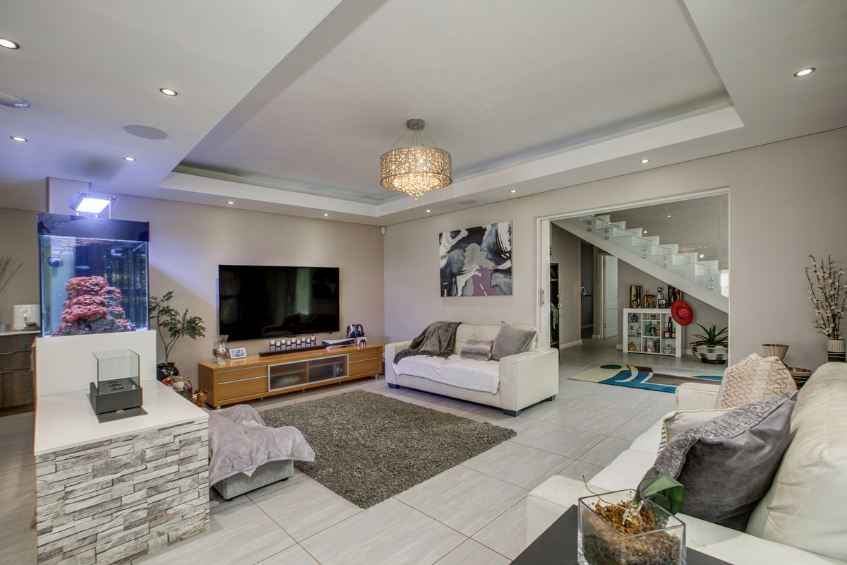 Spacious living room featuring a modern tray ceiling with recessed lighting, tiled flooring, and an open-plan layout leading to a staircase.