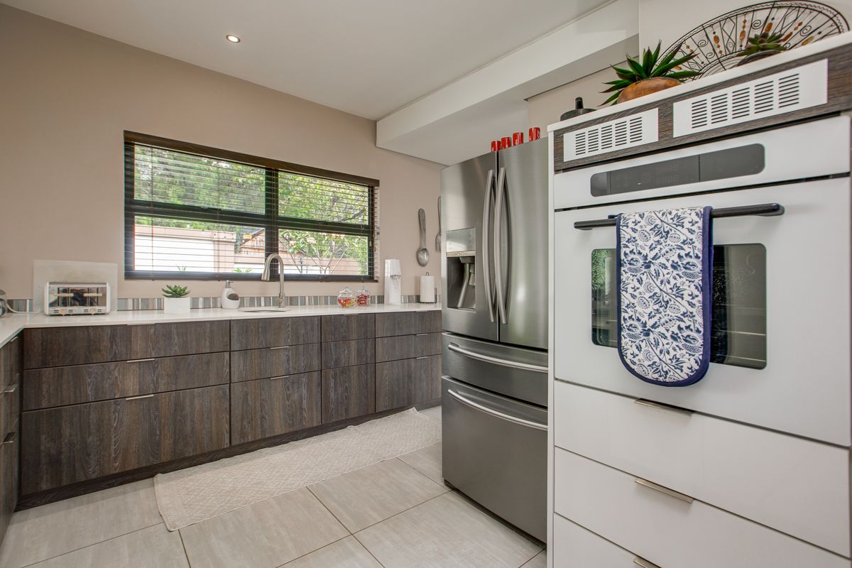 Modern kitchen featuring dark wood-grain cabinetry, white countertops, stainless steel appliances, and a built-in wall oven.