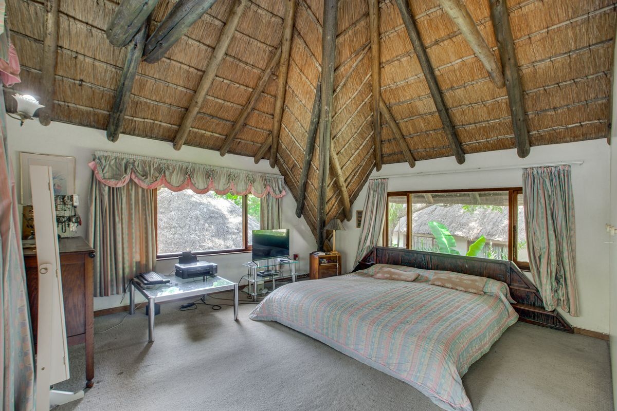 Spacious bedroom featuring a high vaulted thatched ceiling with exposed timber beams and large windows providing natural light and garden views.