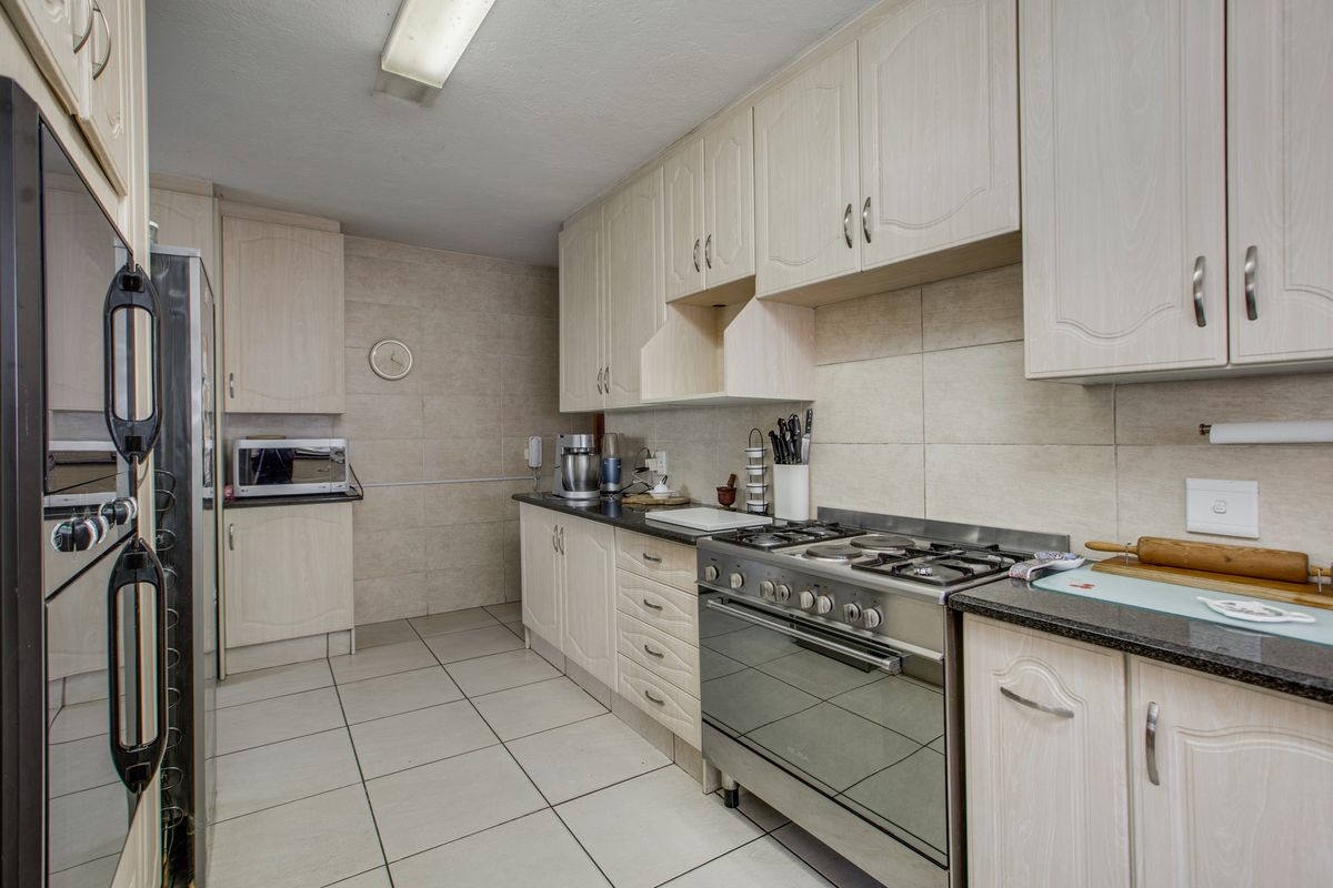 A functional kitchen featuring light-toned cabinetry, granite countertops, a gas hob, and a built-in oven, complemented by tiled flooring and walls.