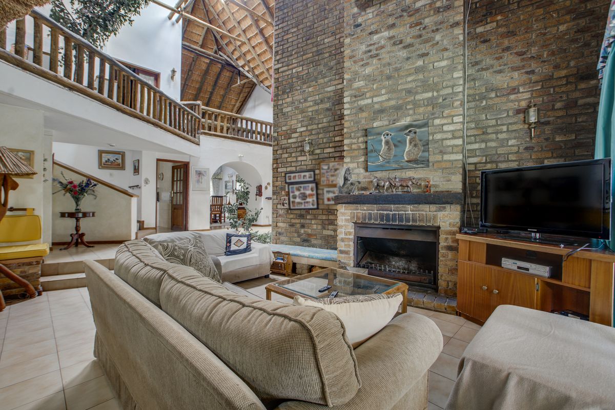 Spacious living room featuring a double-volume thatched ceiling, a prominent floor-to-ceiling brick fireplace, and a mezzanine level overlooking the main area.