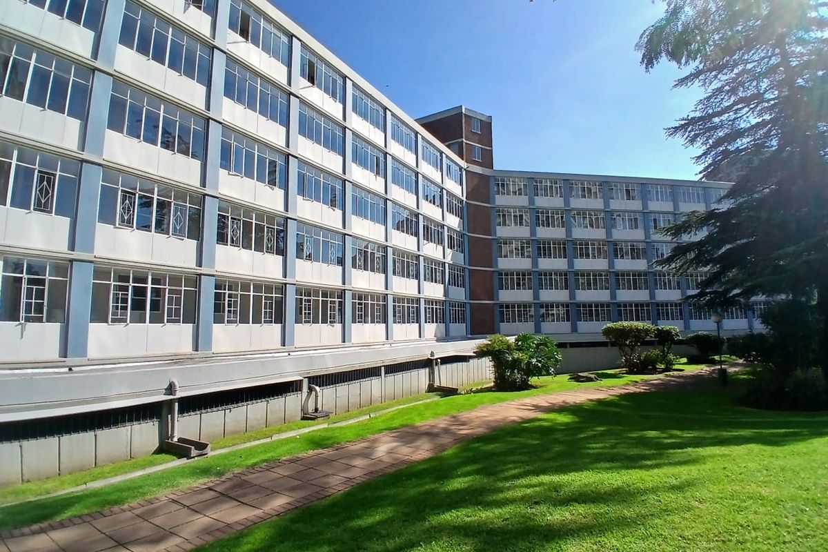 Exterior view of a multi-story apartment building featuring large windows, a paved walkway, and surrounding landscaped garden areas.