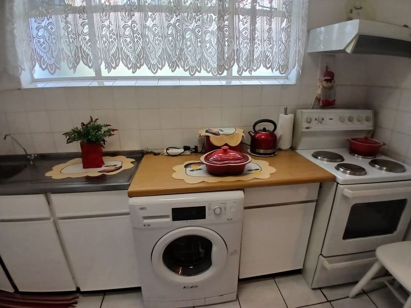 Compact kitchen featuring a built-in sink, wooden countertop, integrated washing machine space, and a freestanding electric stove with an extractor fan.