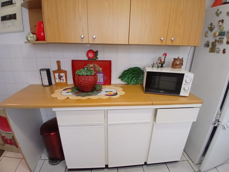 A functional kitchen area featuring light wood-toned upper cabinetry, white lower cabinets, a laminate countertop, and tiled splashback.