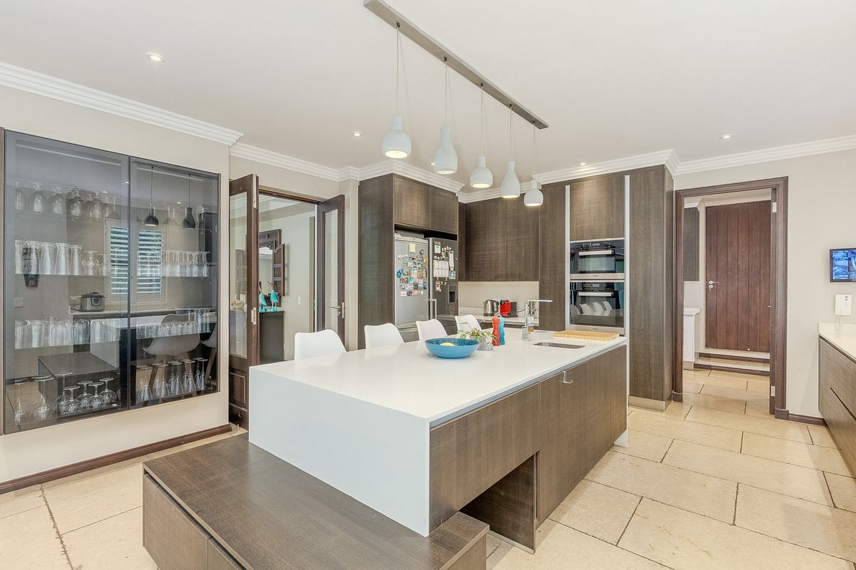 Modern kitchen featuring a large central island with stone countertop, dark wood cabinetry, built-in double ovens, and integrated glass-front display cabinetry.