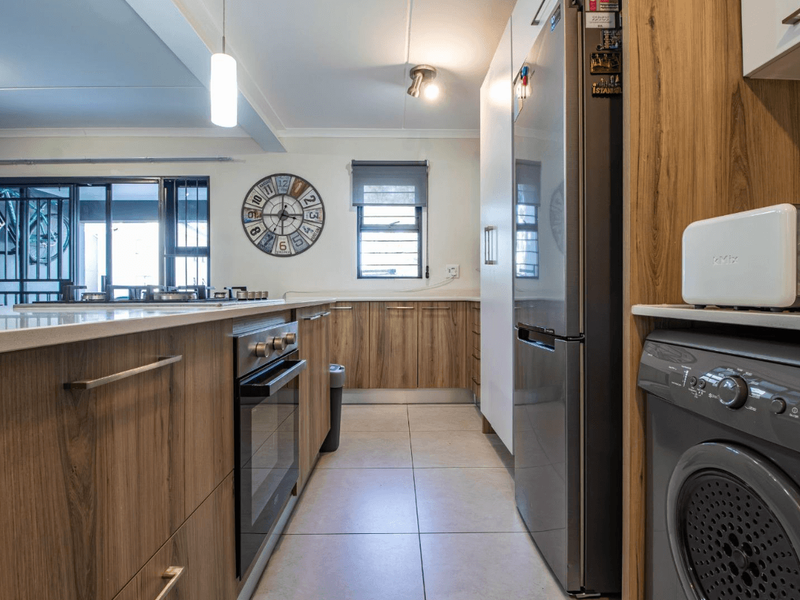 Modern kitchen featuring wood-grain cabinetry, stone countertops, built-in oven, and integrated laundry appliances, flowing into an open-plan living area.