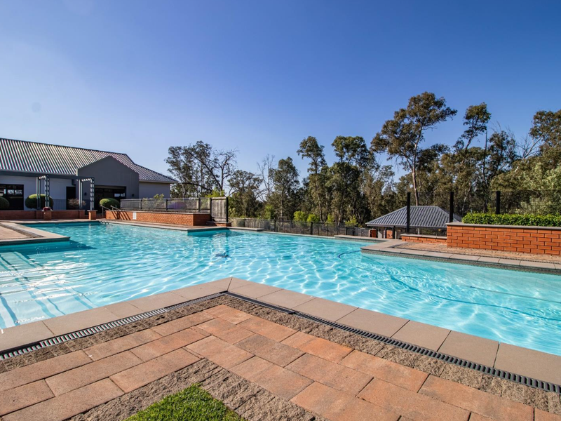 A well-maintained swimming pool area featuring paved surrounds, brick retaining walls, and a clear view of the surrounding landscape.