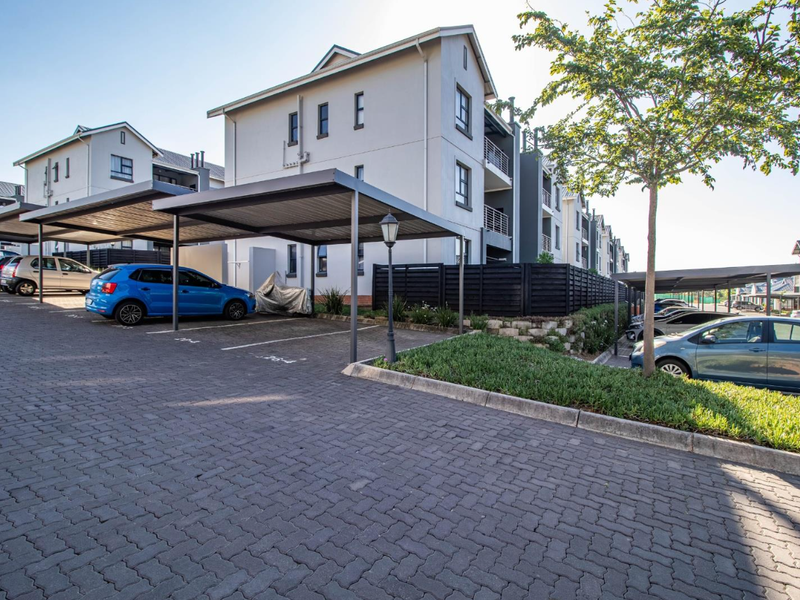 Exterior view of the townhouse complex featuring paved parking areas with covered carports and landscaped garden beds.
