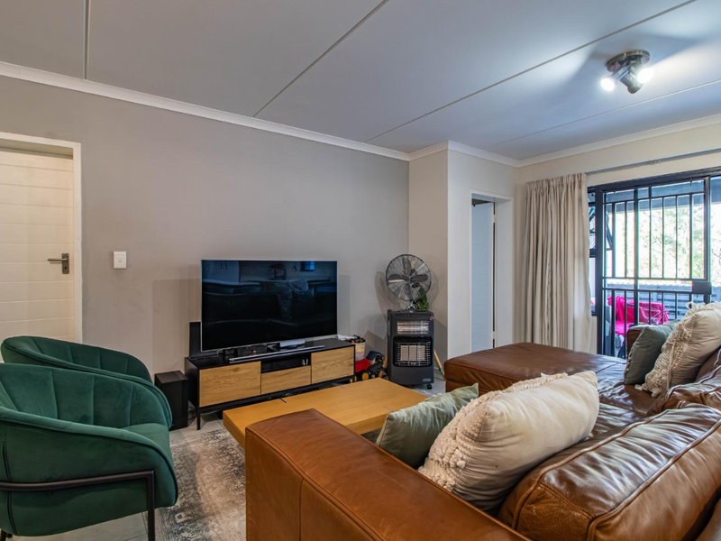 A comfortable living room featuring tiled flooring, neutral wall tones, and sliding glass doors that provide access to an outdoor balcony area.