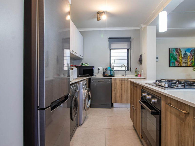 Modern kitchen featuring wood-grain cabinetry, stone countertops, built-in oven, gas hob, and integrated laundry appliance connections.