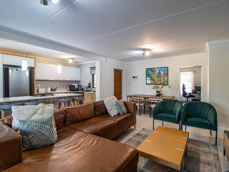 Open-plan living area featuring a modern kitchen with breakfast bar, dining space, and lounge, finished with tiled flooring and neutral tones.