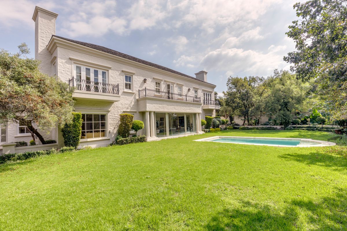 A spacious rear garden featuring a well-maintained lawn, a swimming pool, and a classic two-story residence with balconies and large glass doors.