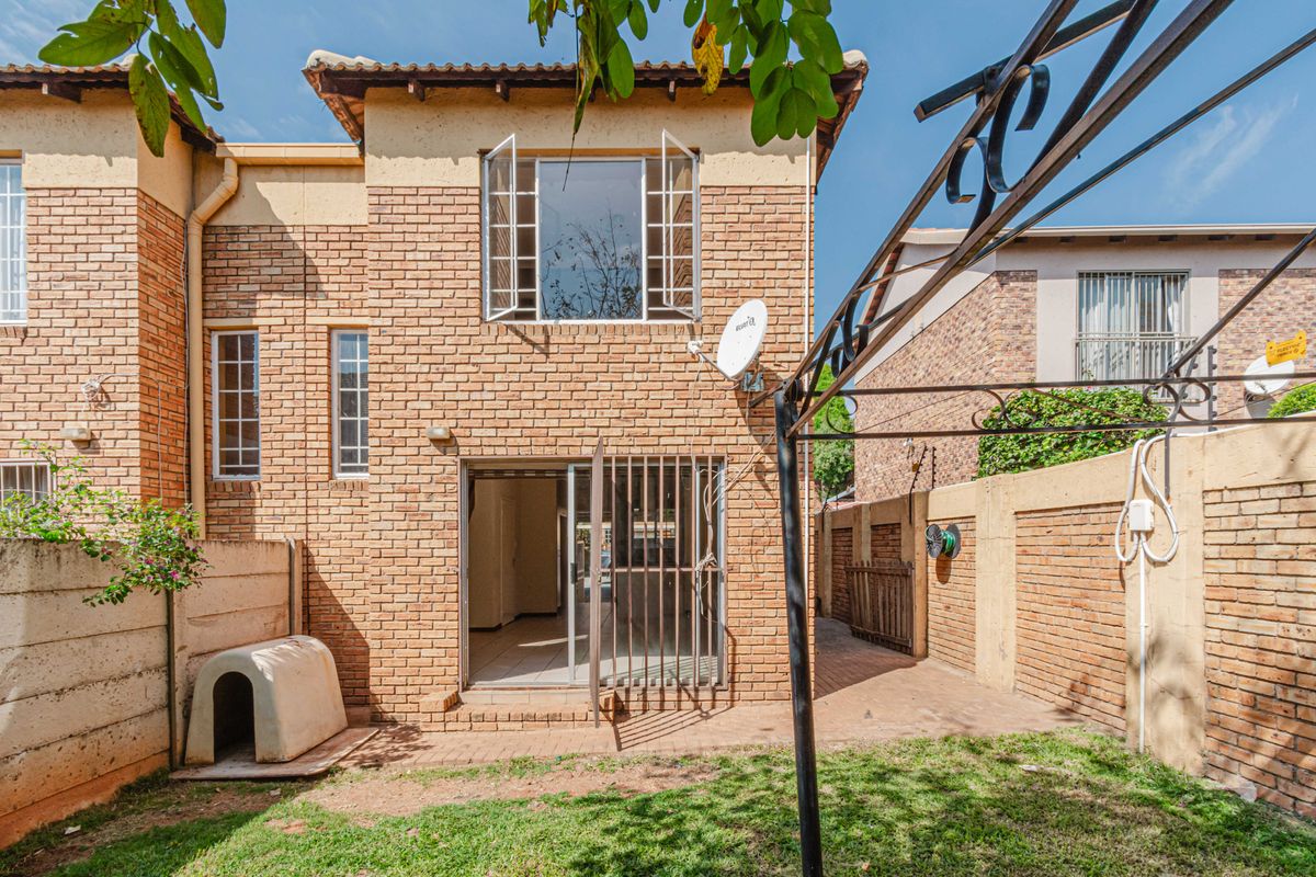 Rear view of a double-story brick townhouse featuring a small private garden, paved patio area, and secure metal security gate at the entrance.