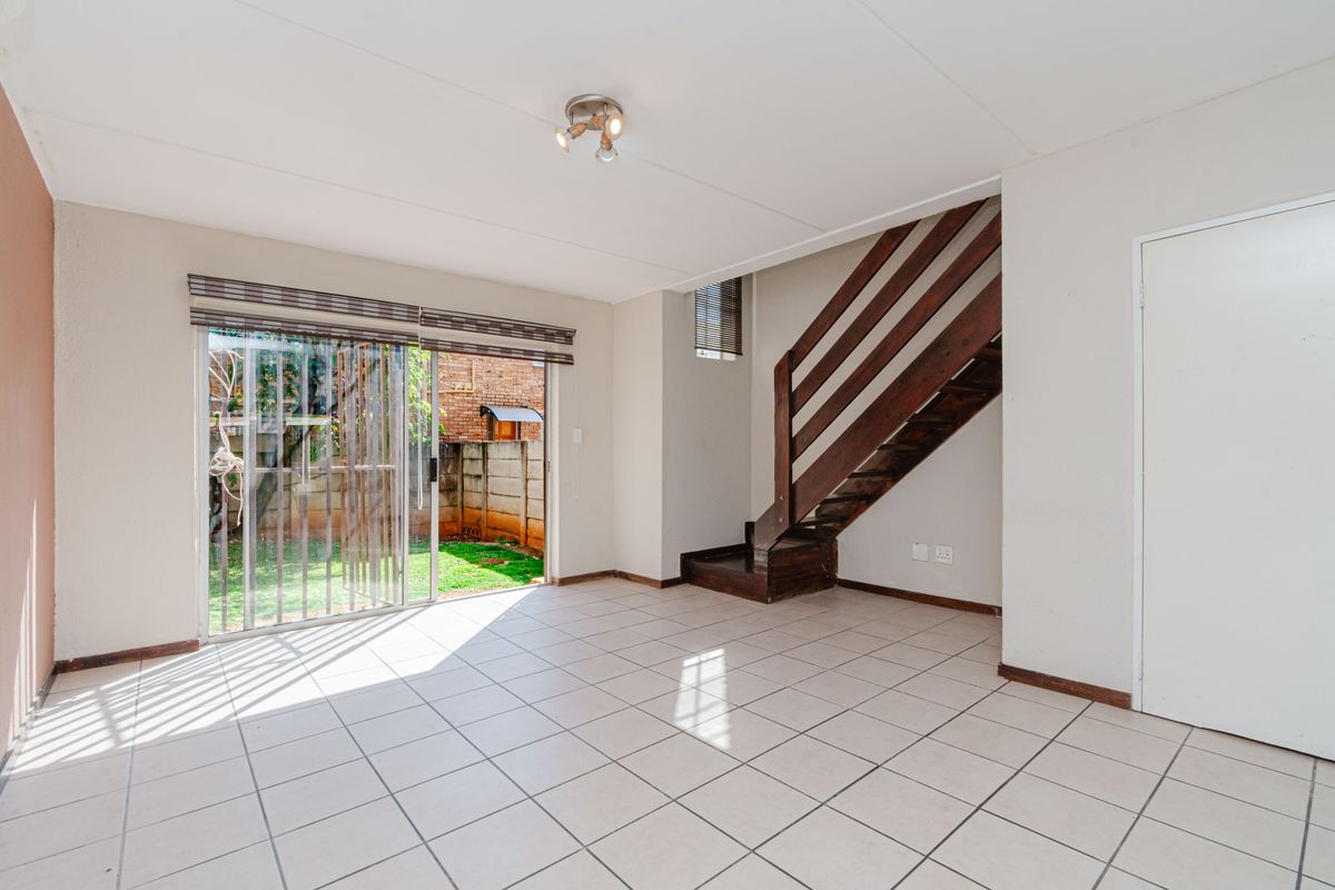 An open-plan living area featuring tiled flooring, a wooden staircase, and sliding glass doors providing direct access to the rear garden.